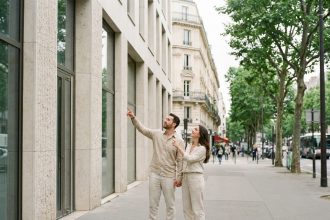Couple visitant un immeuble neuf dans le 12e arrondissement de Paris, façade contemporaine en pierre et verre, ambiance urbaine parisienne